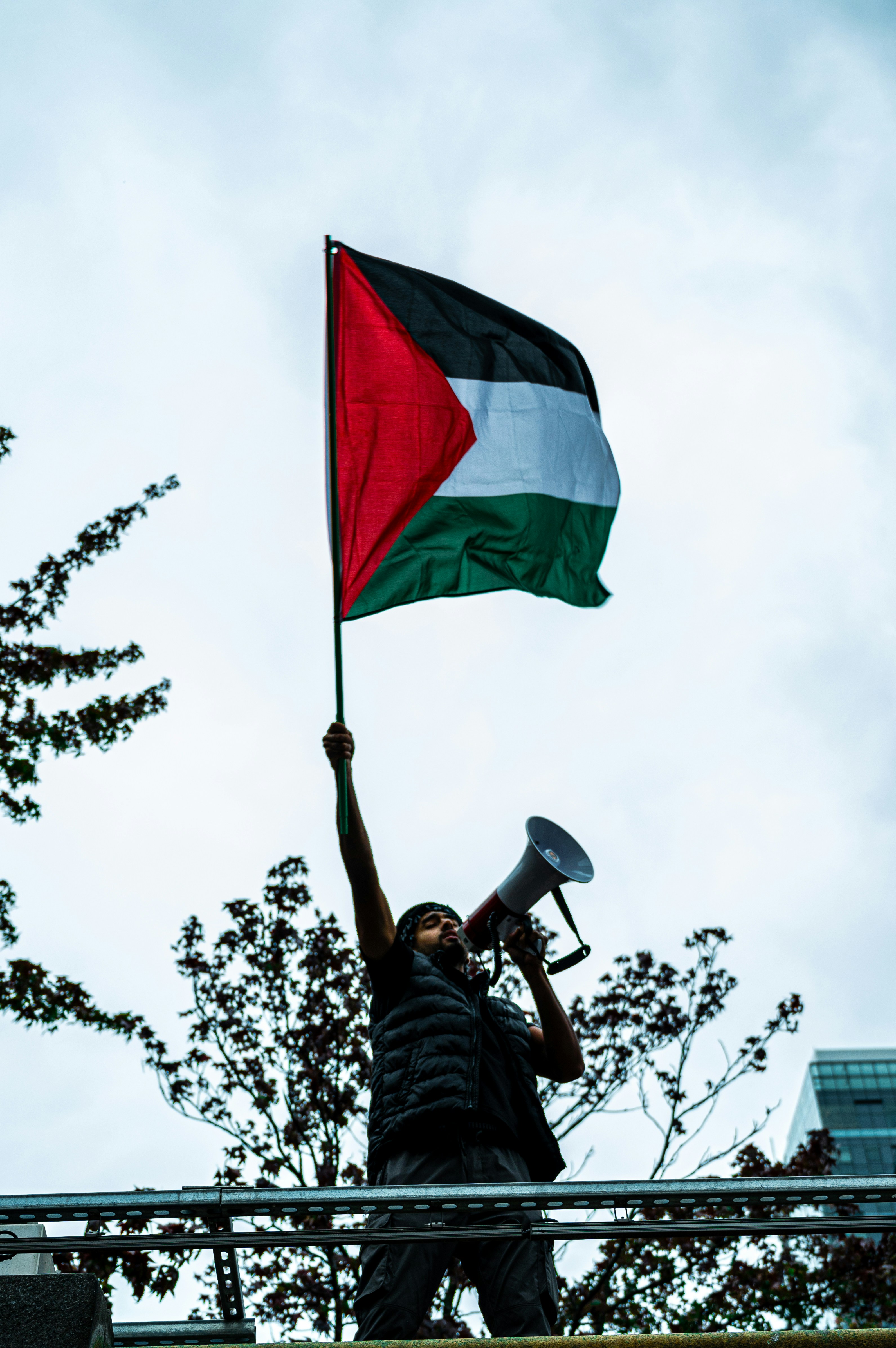A protestor holds a Palestinian flag and a megaphone, vocally symbolizing active resistance.